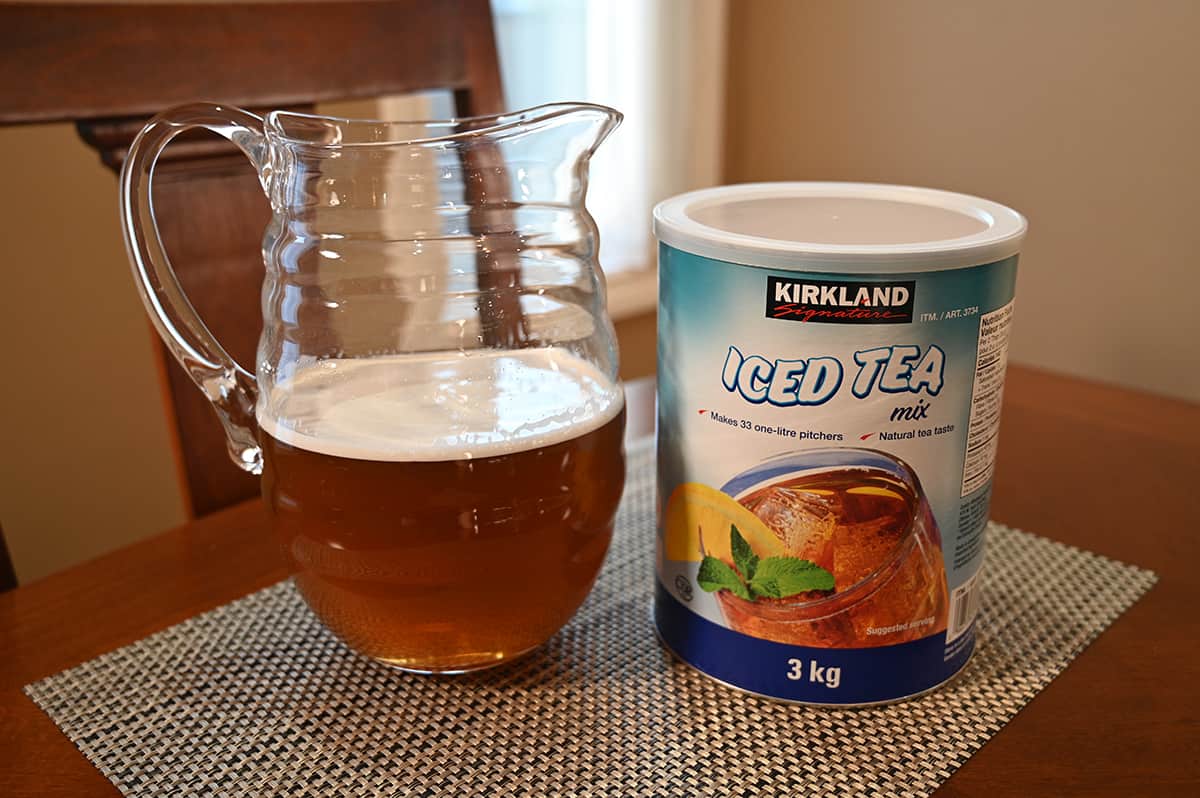 Image of a pitcher of prepared iced tea next to the iced tea mix container sitting on a table.