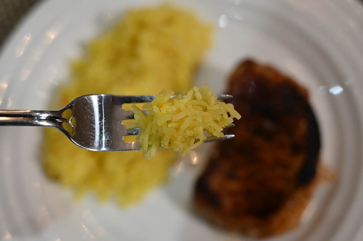 Closeup image of a fork with saffron rice loaded on it with a plate of rice and a pork chop in the background of the image.