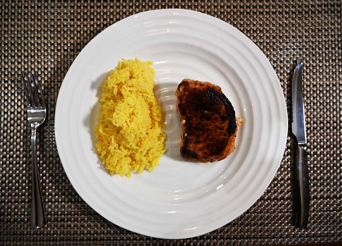 Top down image of a plate of rice with a pork chop beside it.
