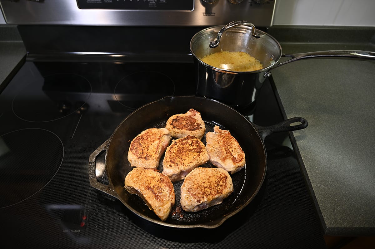 Image of a stovetop with pork chops cooking in a skillet and rice cooking in a pot.