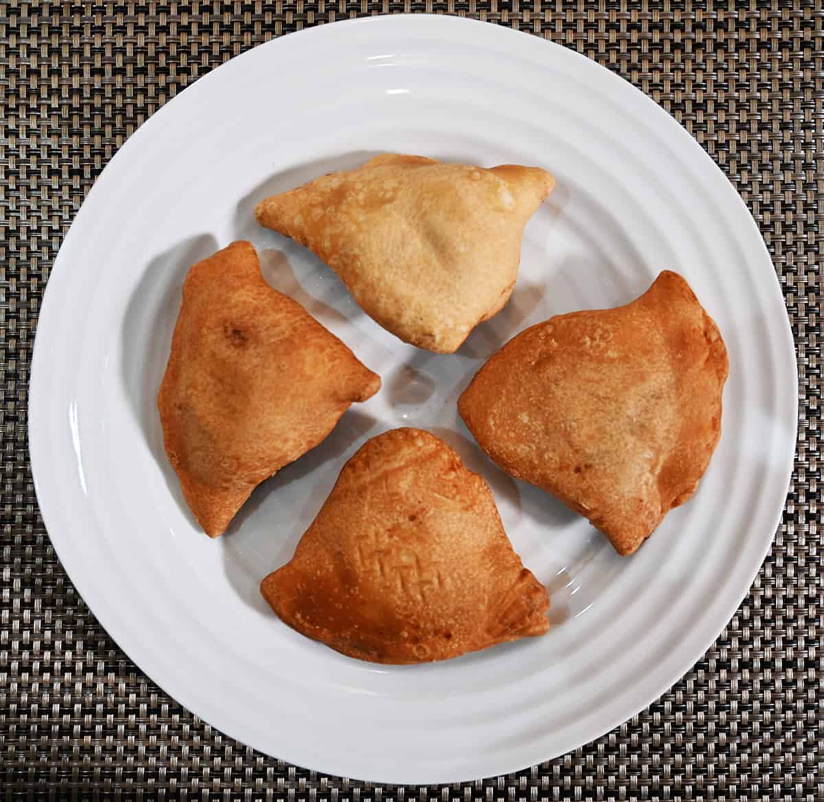 Top down image of four baked samosas served on a white plate.