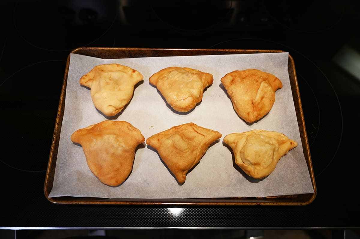 Image of six samosas on a baking sheet lined with parchment paper.