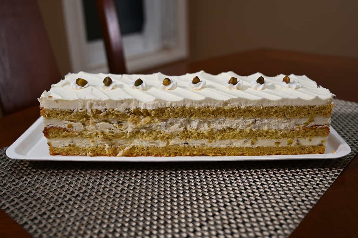 Side view image of the pistachio cake with the lid off so the entirety of the cake is visible.