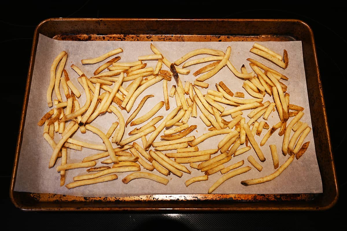Top down image of a cookie sheet lined with parchment paper with frozen fries on the paper about to be baked.