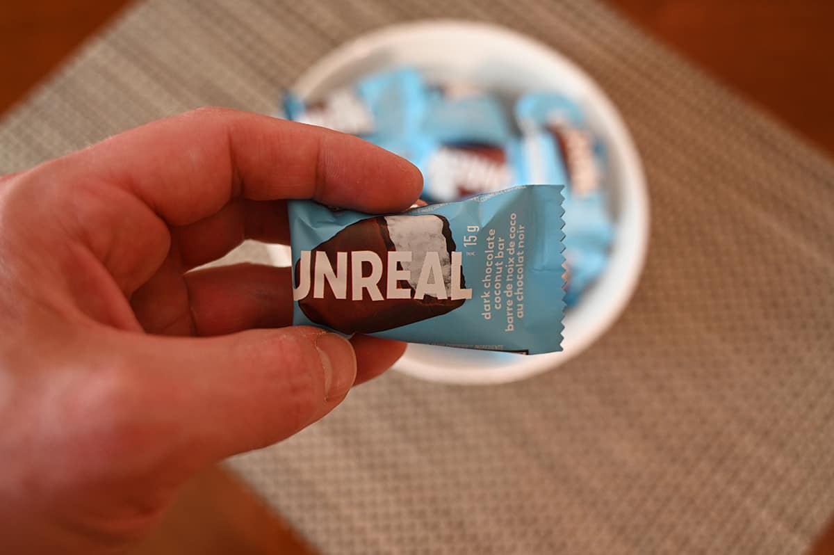 Closeup image  of a hand holding one wrapped coconut mini bar in front of the camera.