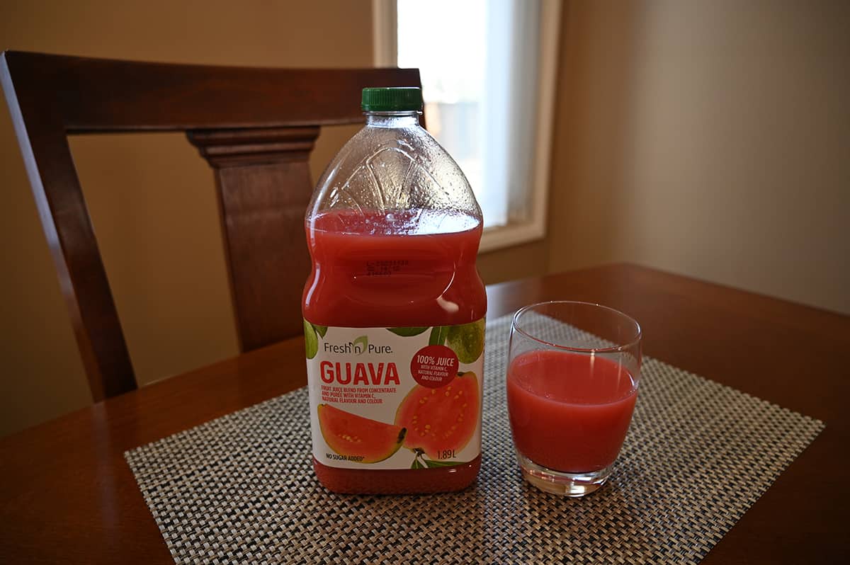 Image of the bottle of juice guava juice standing beside a glass of poured juice on a table.