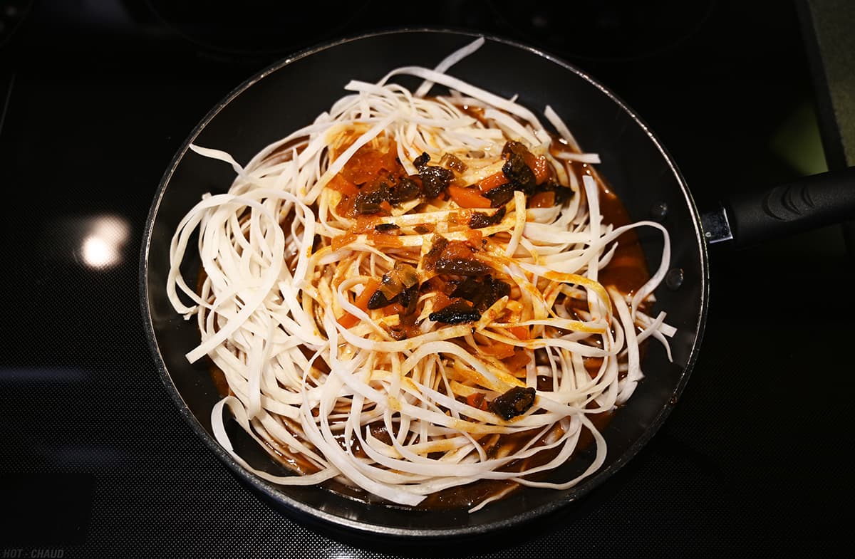 Image of rice noodles with sauce poured over them in a pan prior to stir frying.