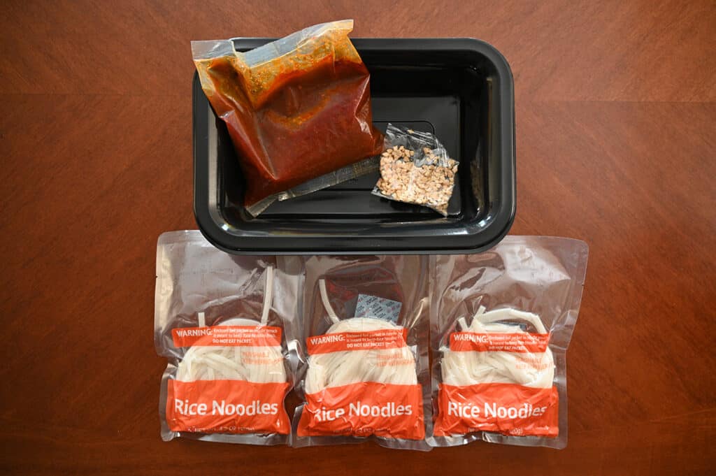 Top down image showing everything that comes in the package, noodles, sauce, peanut pieces and a microwaveable tray.