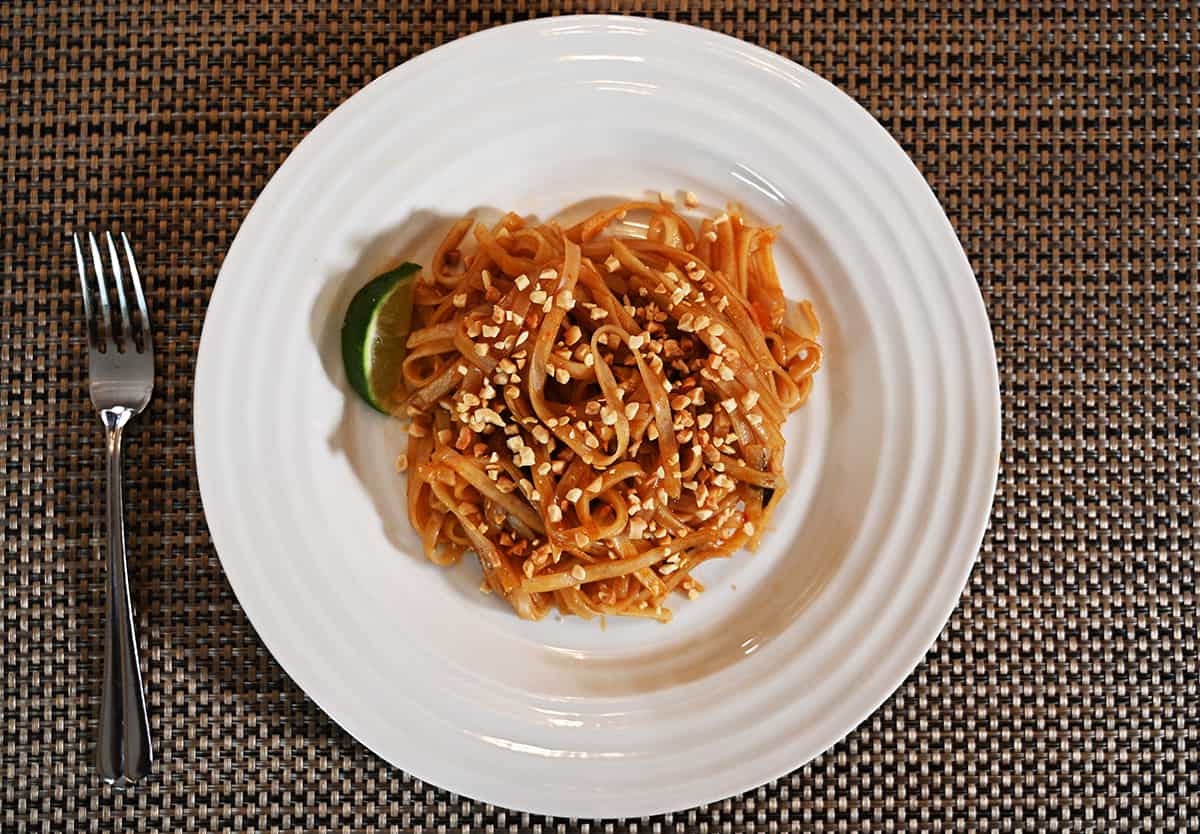 Top down image of the Pad Thai cooked and served on a white plate with a sprinkle of peanuts on top and a slice of lime beside the noodles.