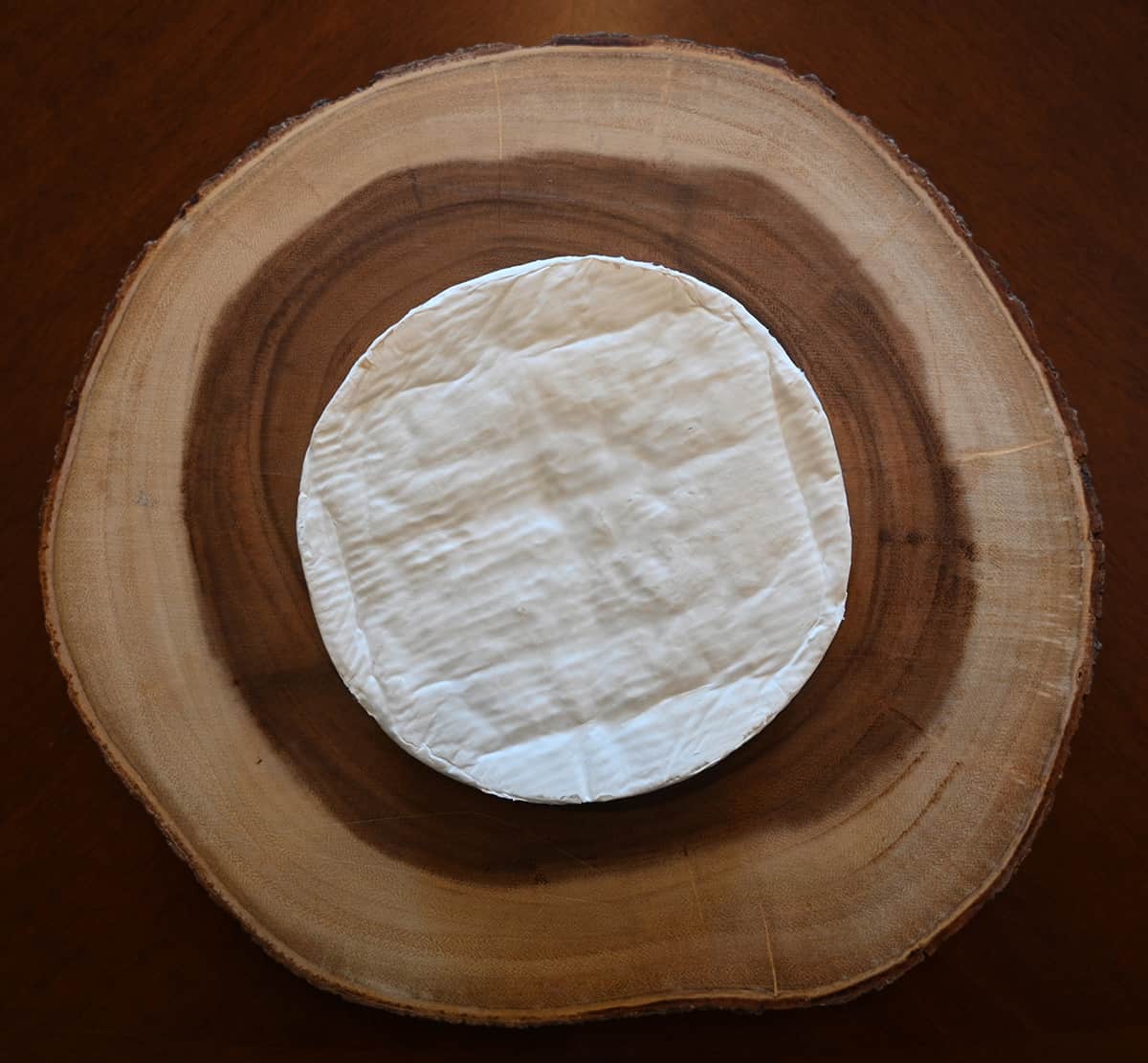 Top down image of the Brie unwrapped from the packaging and with the rind on, served on a wood charcuterie board.