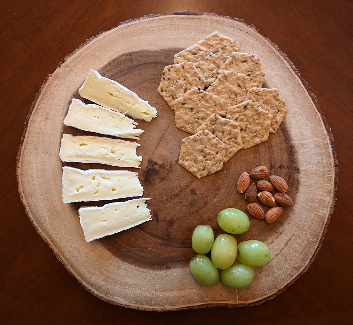 Top down image of a cheese board with Brie, crackers, almonds and grapes on it.