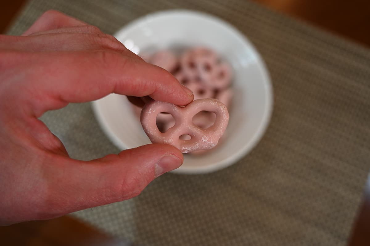 Closeup image of a hand holding one strawberry yogurt pretzel over a bowl of strawberry pretzels.