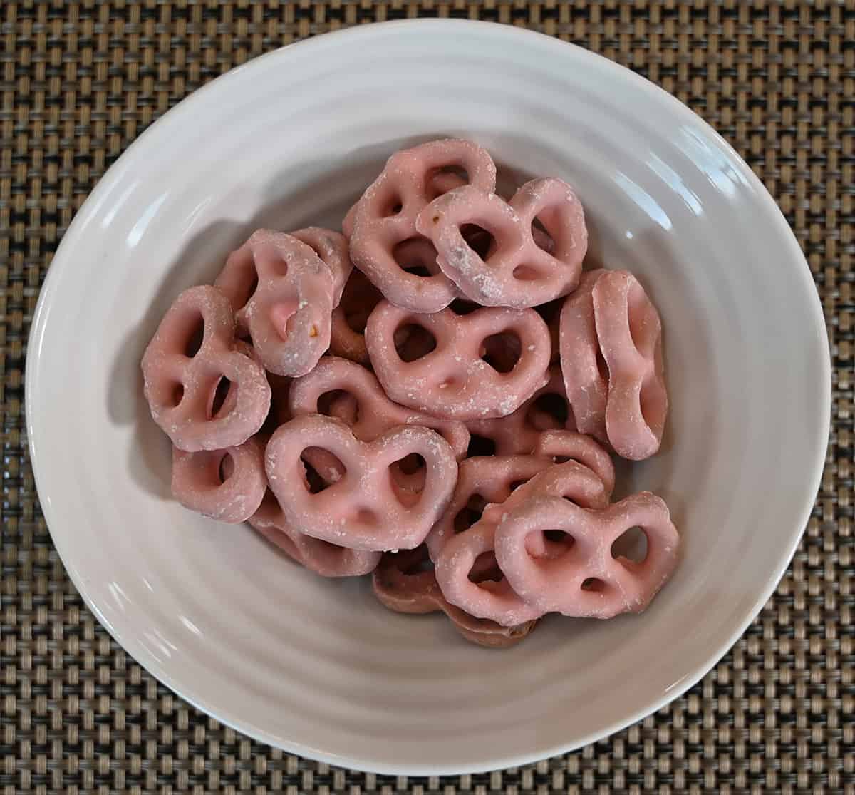 Top down image of a bowl of strawberry covered pretzels sitting on a placemat.