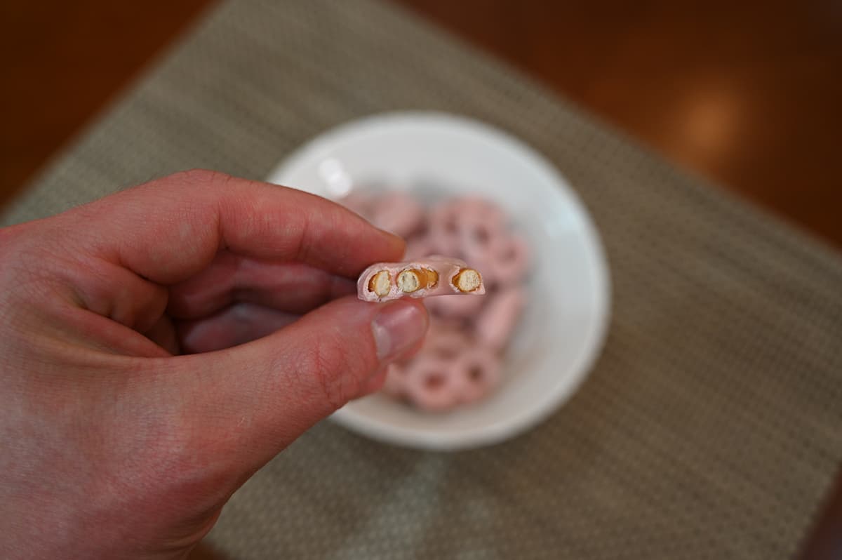 Closeup image of one pretzel with a bite taken out of it with a bowl or pretzels in the background.