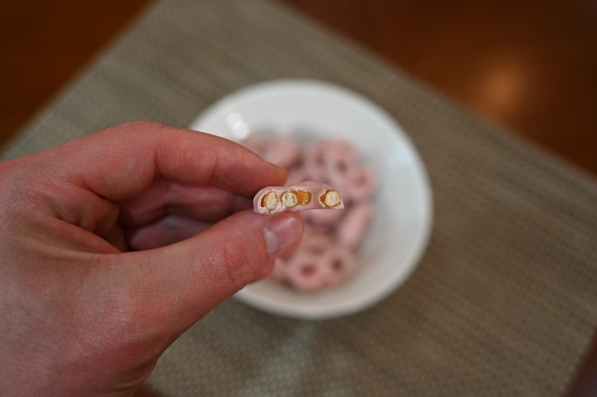 Closeup imasge of a hand holding one strawberry yogurt pretzel with a bite taken out of it so you can see the inside of the pretzel.