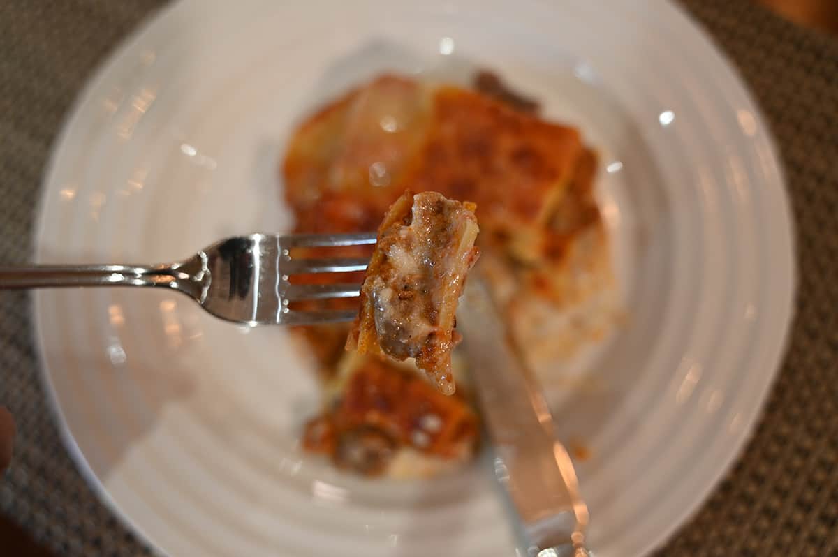 Closeup image of one bite of lasagna on a fork with the plate of lasagna in the background.