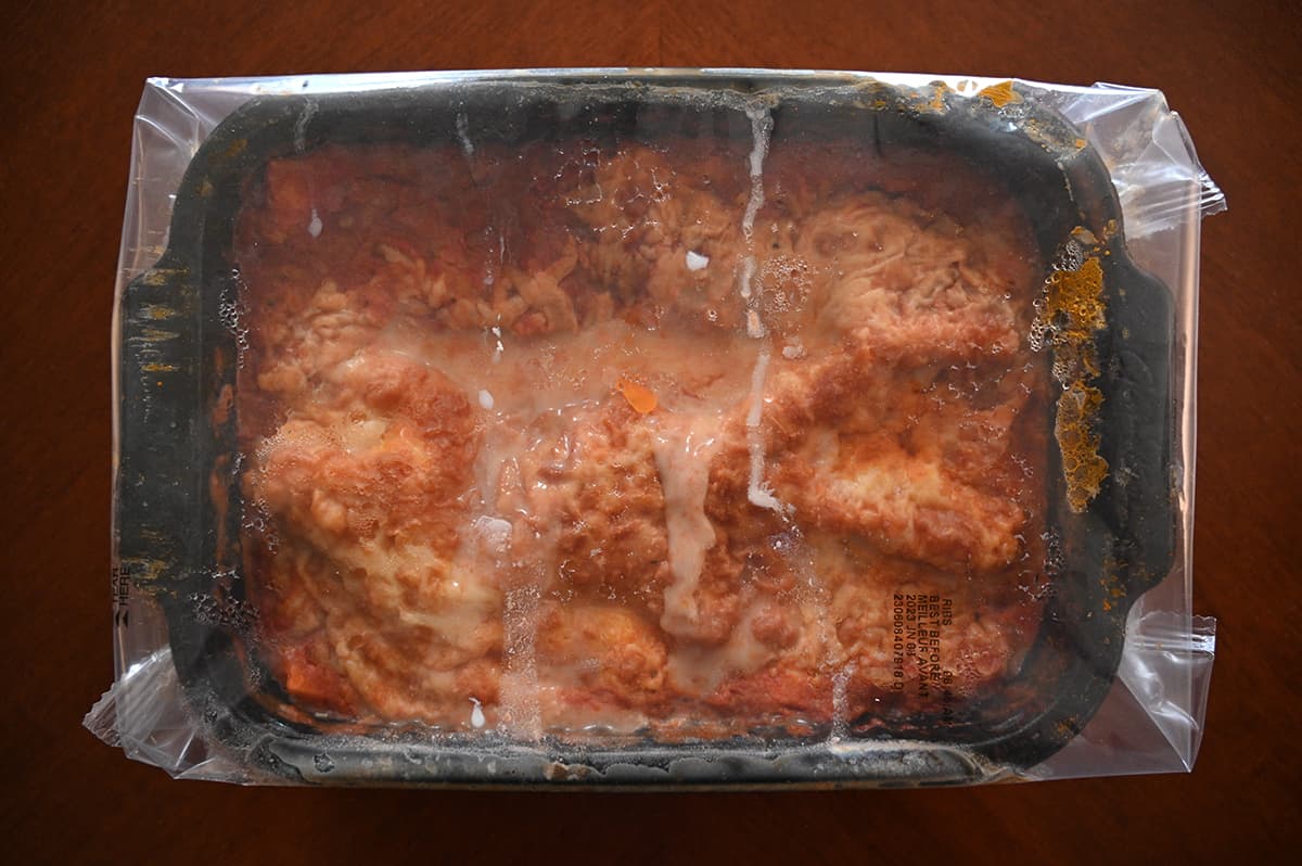 Image of the lasagna before cooking in the tray with plastic wrap on top.