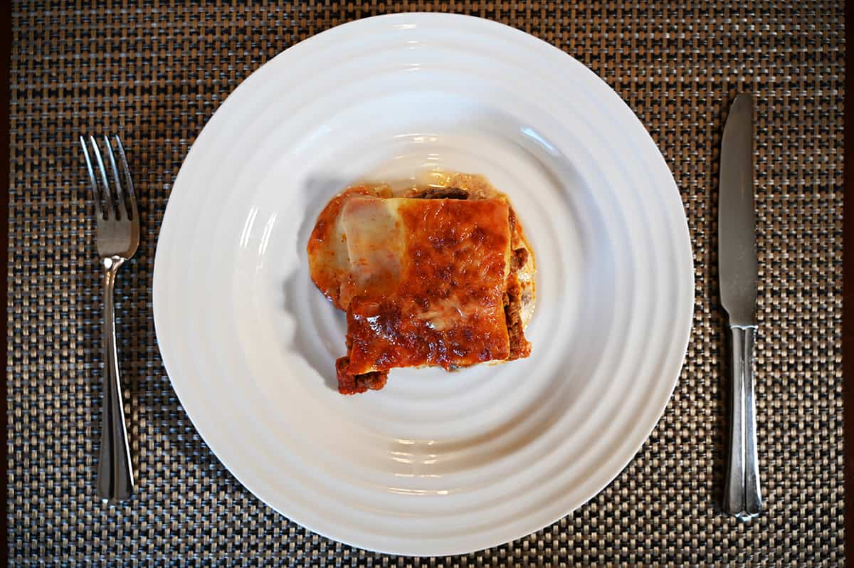 Top down image of one slice of lasagna served on a white plate with a fork and knife beside it.