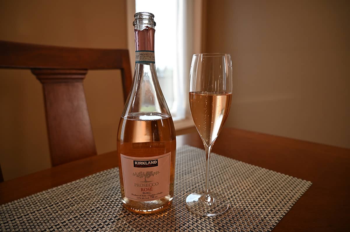 Image of the bottle of rose open, beside a tall thin stemmed clear glass with rose poured into it.