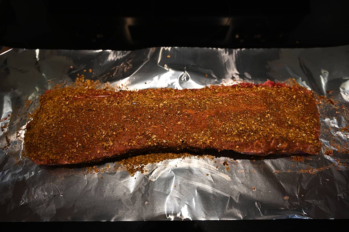 Image of a rack of raw pork ribs rubbed with the seasoning on them laying on aluminum foil.