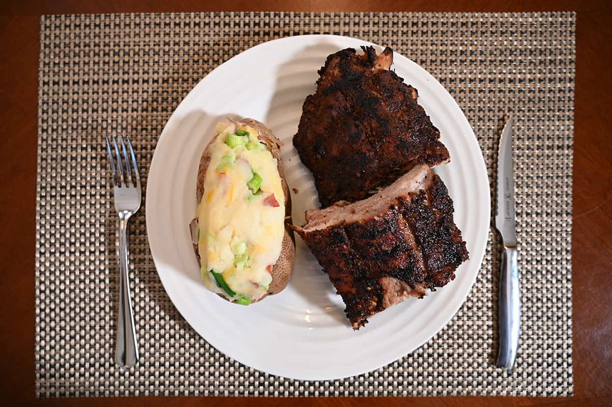Top down image of a  white plate with a double stuffed potato beside two large servings of ribs. There's a fork and knife beside the plate.