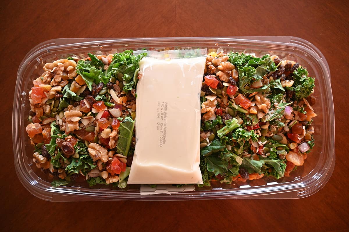 Top down image of the salad on a table with the lid off. The salad has a full packet of salad dressing resting on top of it.
