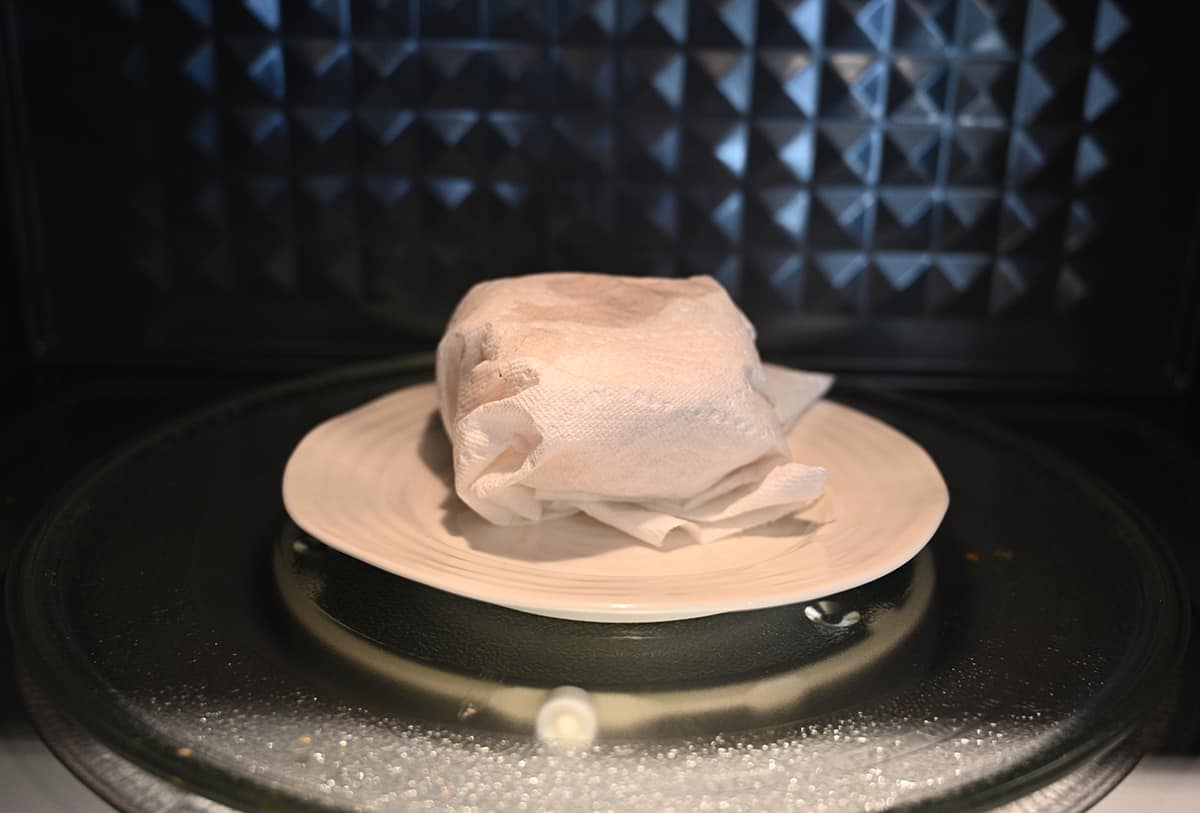 Image of one breakfast sandwich, wrapped in paper towel and sitting on a plate in the microwave, ready to heat.