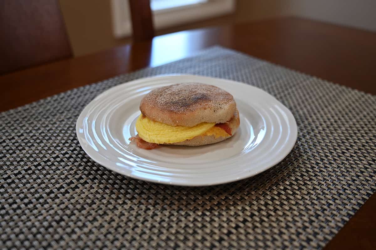 Image of one heated breakfast sandwich served on a white plate, sitting on a dining table.