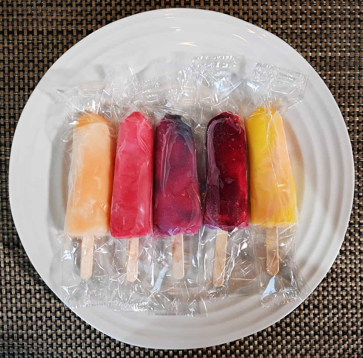 Top down image of all five flavors of popsicles that come in the box on a plate in their clear plastic packaging.