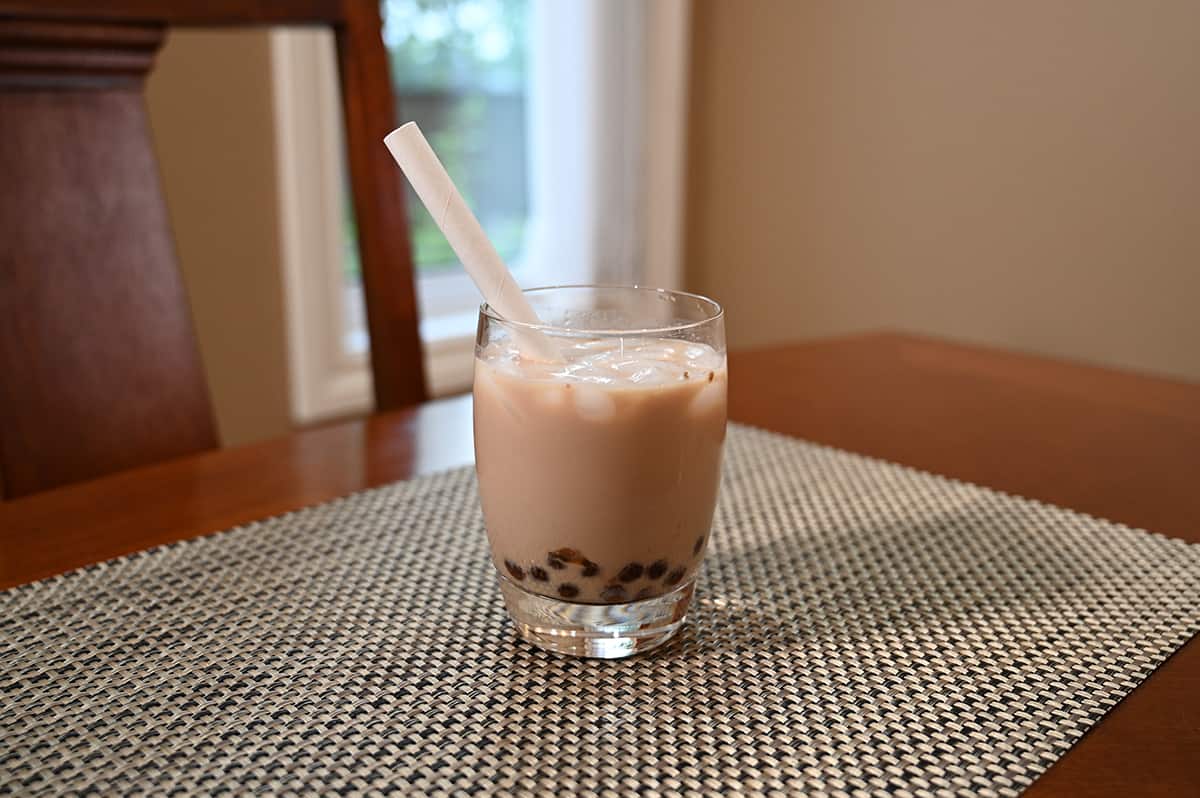 Image of the Crème brûlée milk tea with caramel boba prepared in a clear glass with a straw in it, sitting on a table.