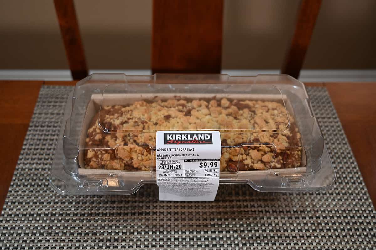 Image of the Costco Kirkland Signature Apple Fritter  Loaf sitting on a table in the plastic container it comes in.