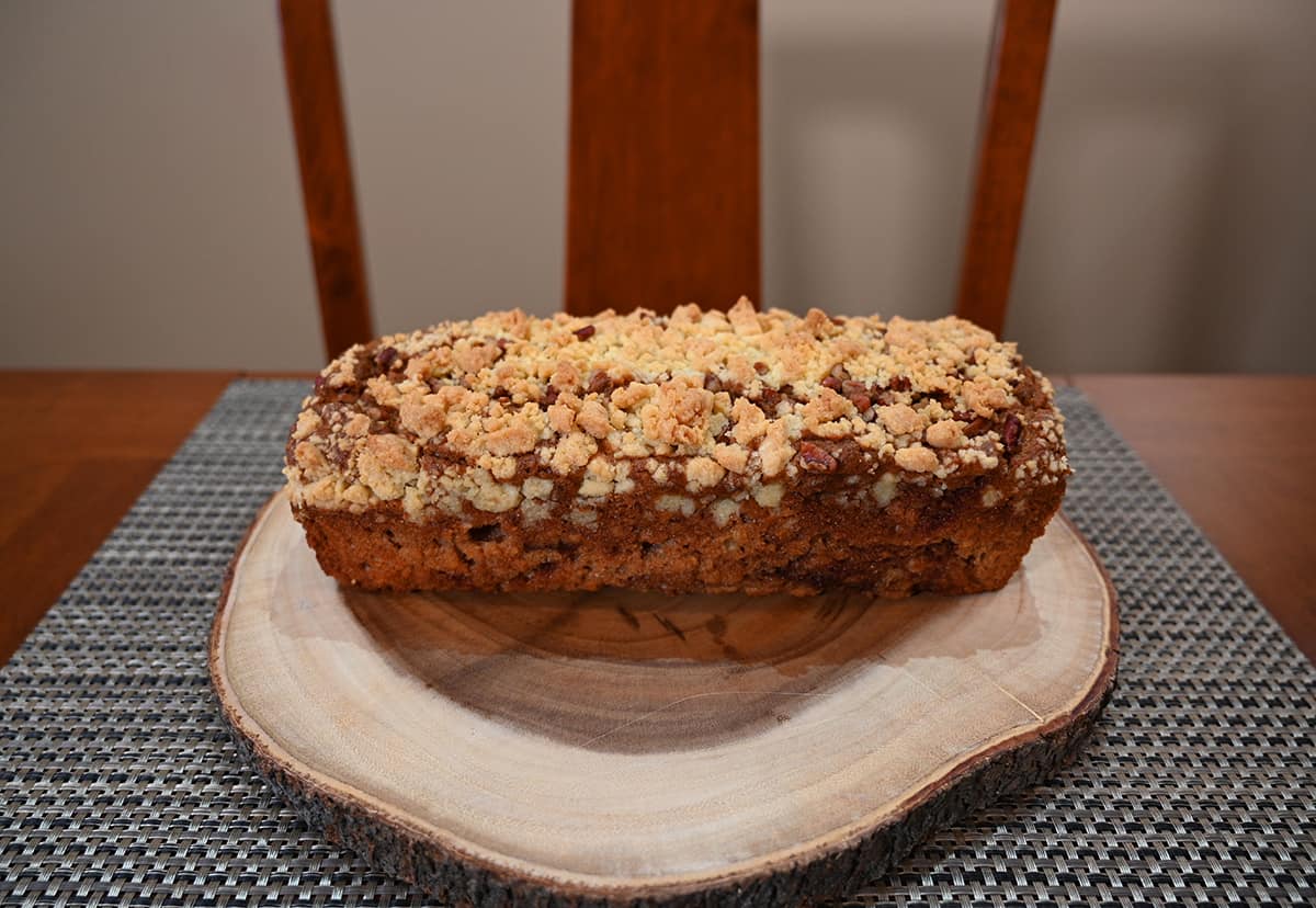 Image of the entire apple fritter loaf out of the package and served on a wood cutting board. There is a streusel topping on the loaf.