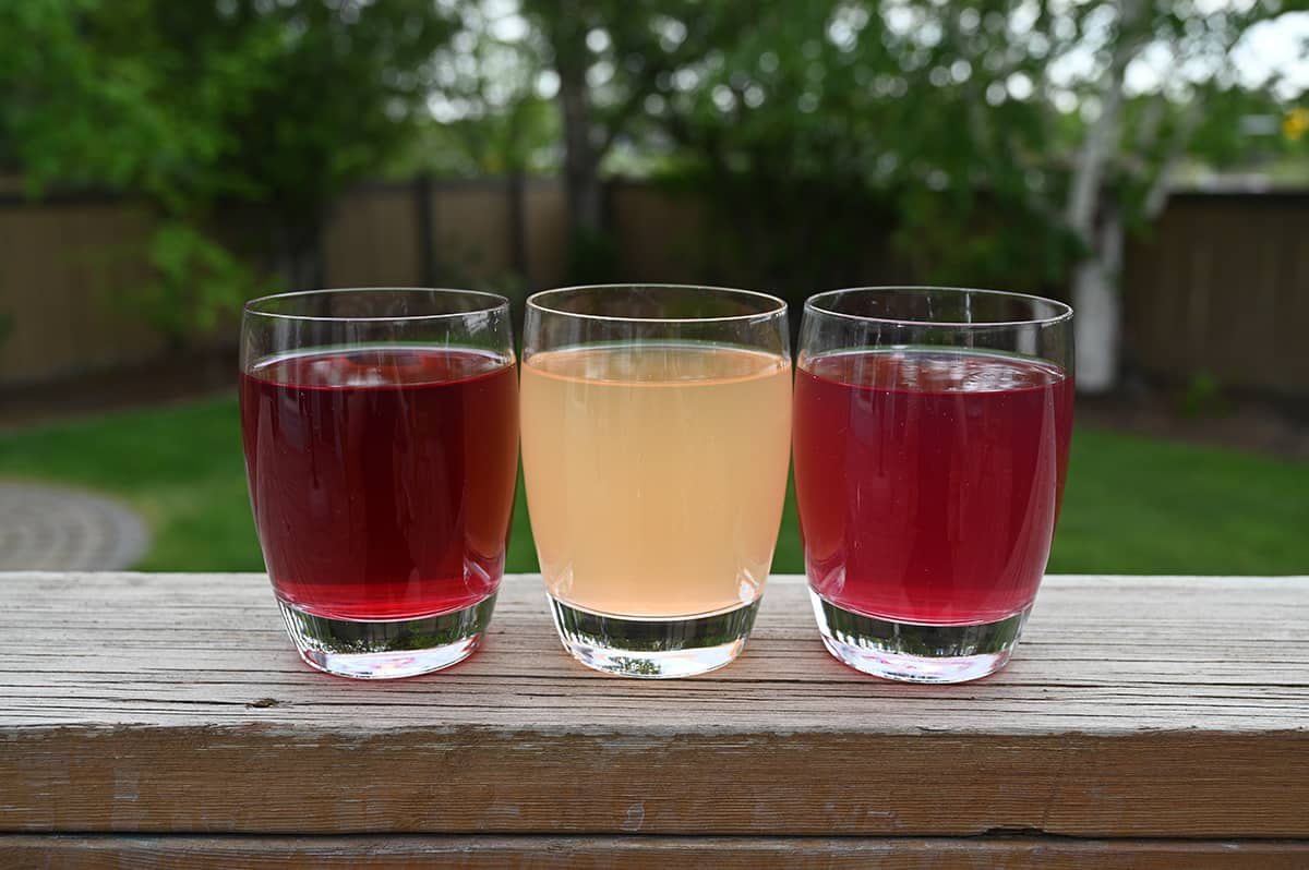 Image of three clear glasses with aspire energy drink poured into them sitting on a table outside. Left to right is raspberry acai, mango lemonade and sweet cherry.