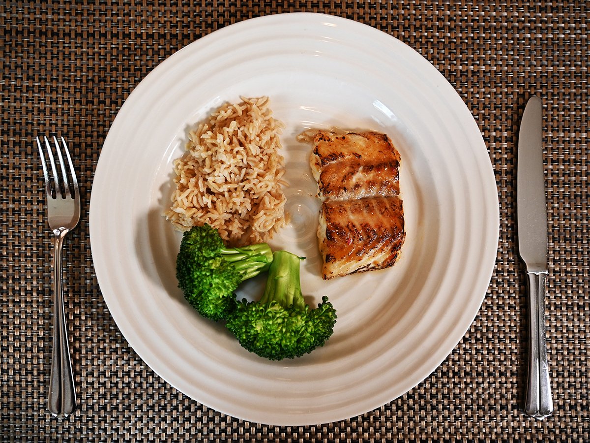 Top down image of a plate with a piece of cod on it beside rice and brocolli.