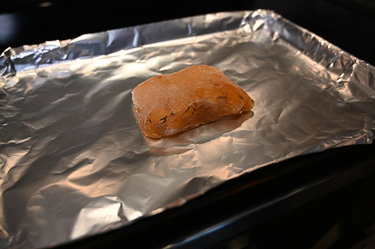 Image of a piece of cod sitting uncooked on a baking tray lined with aluminum foil.