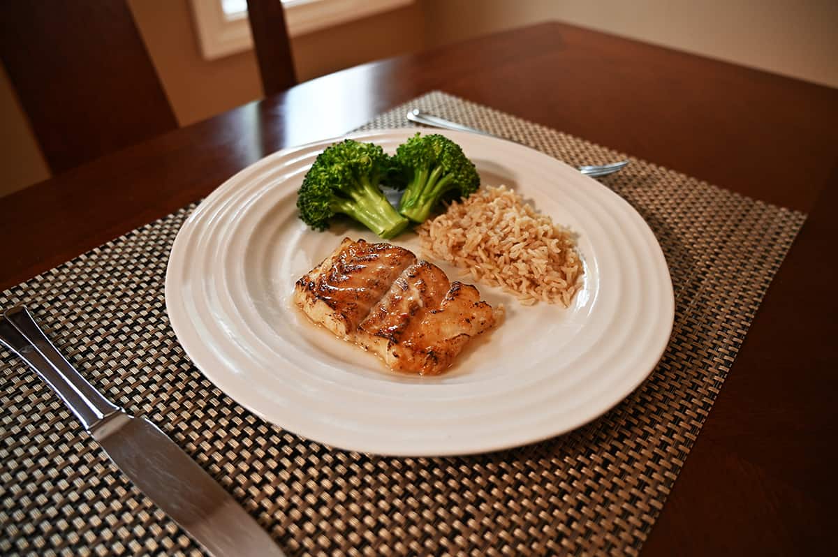 Side view image of a plate with a piece of cod on it beside rice and brocolli.
