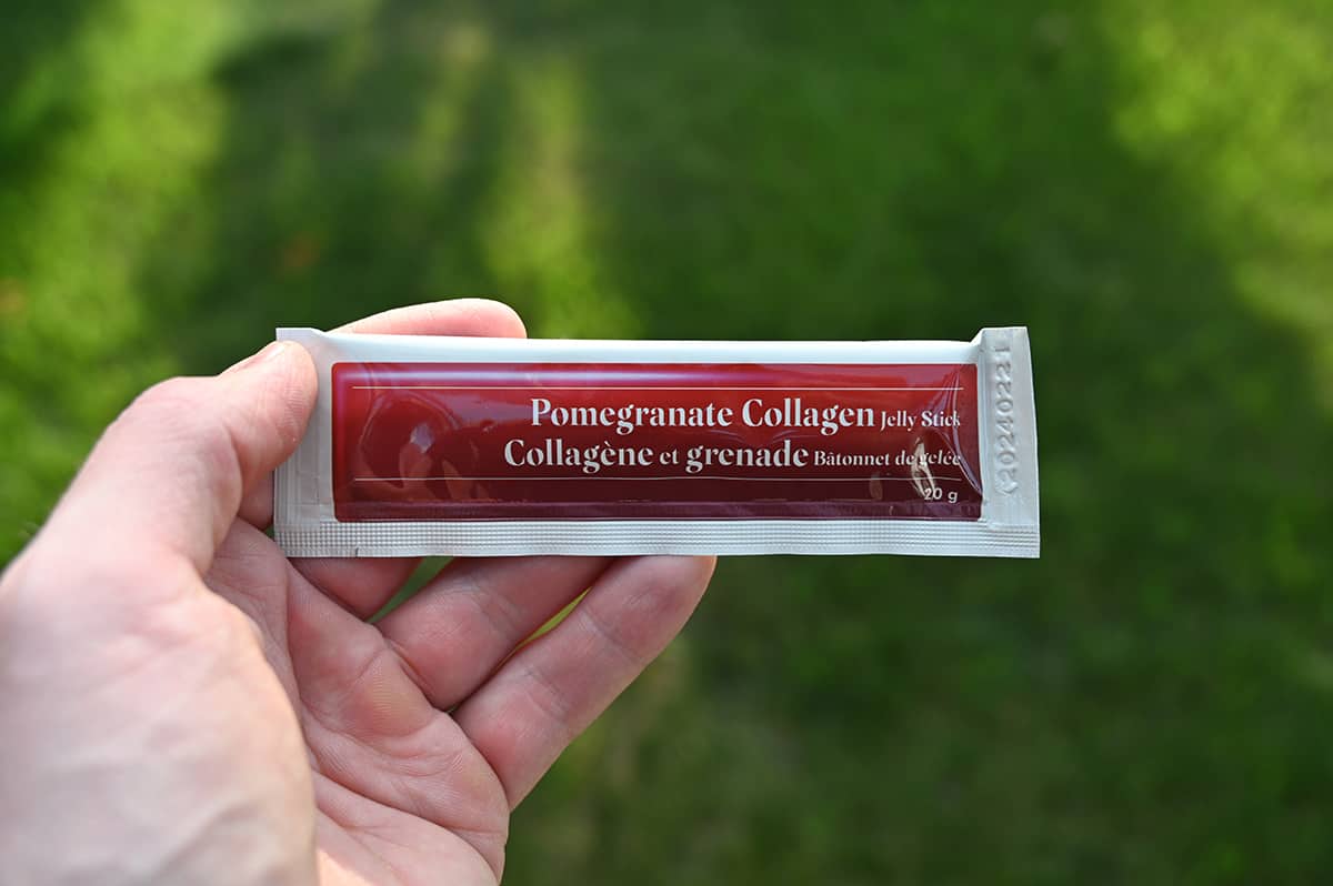 Image of a hand holding one packaged pomegranate collagen jelly stick closeup to the camera.