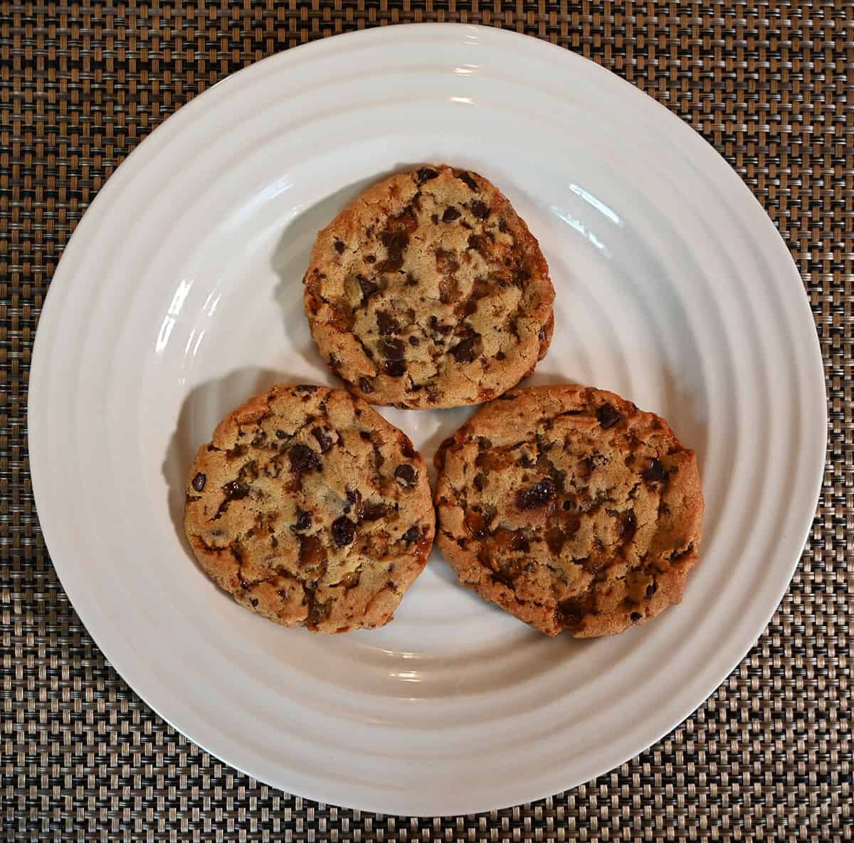 Top down image of three toffee chocolate chip cookies served on a white plate.