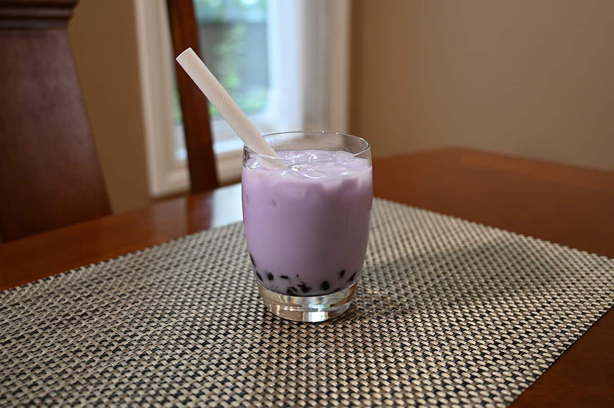 Image of the taro milk tea with brown sugar boba prepared in a clear glass with a straw in it, sitting on a table.