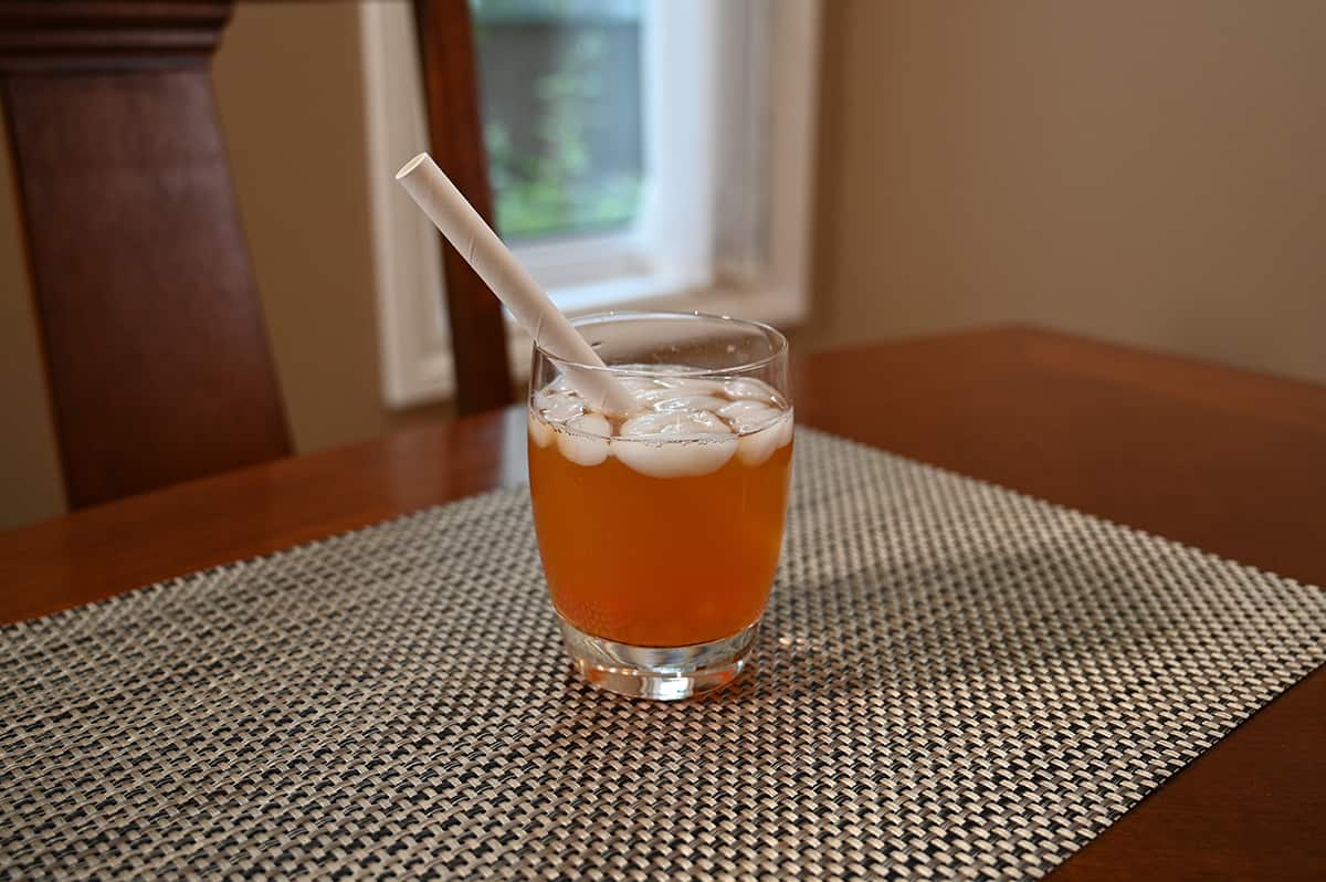 Image of the passion fruit pineapple green tea with fruity boba prepared in a clear glass with a straw in it, sitting on a table.