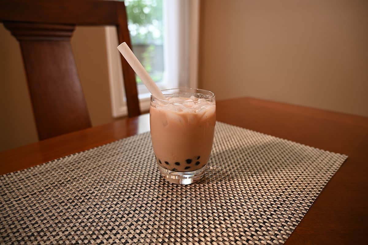 Image of the classic milk tea with brown sugar boba prepared in a clear glass with a straw in it, sitting on a table.