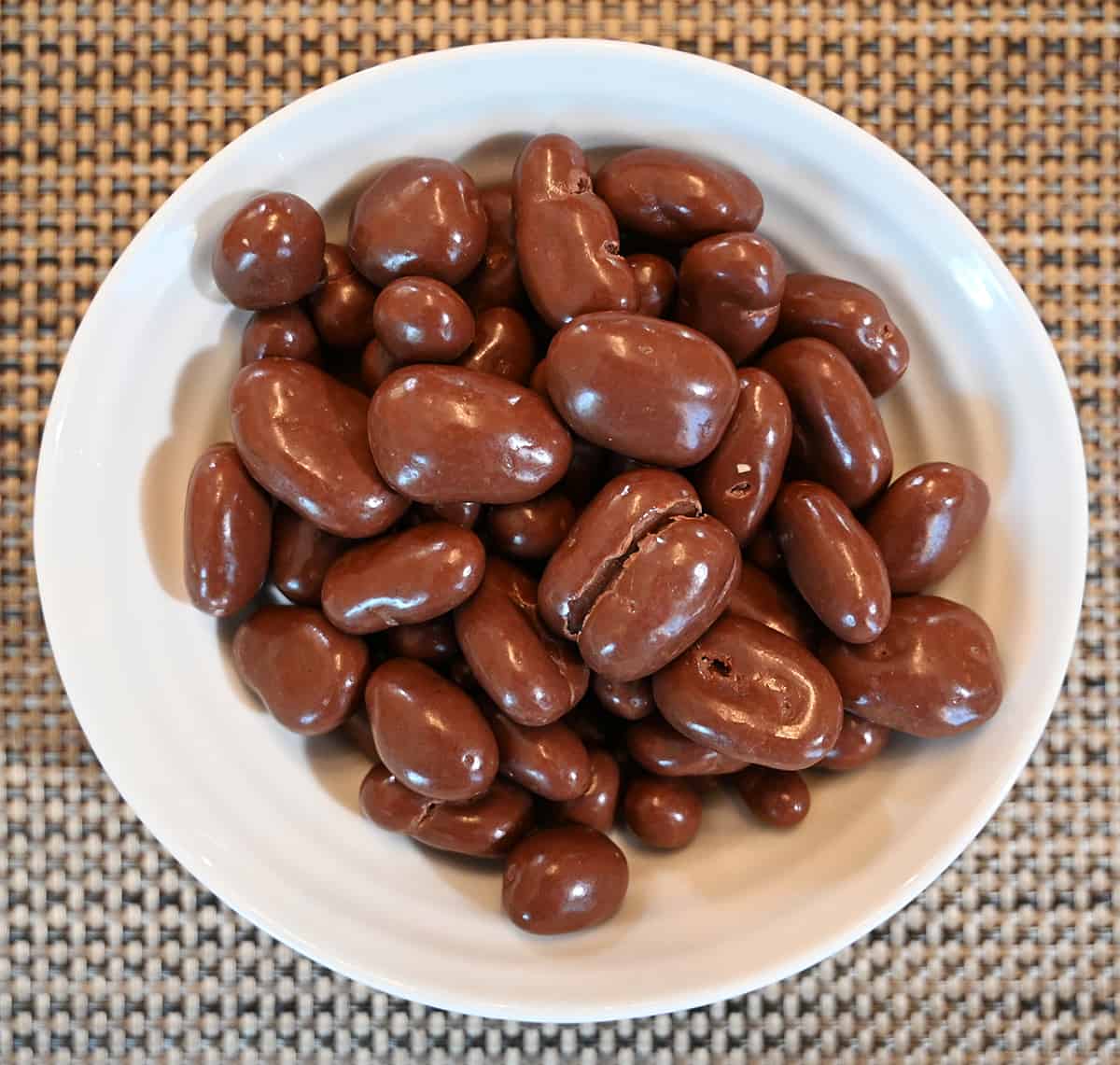 Top down image of the milk chocolate pecans poured into a white bowl that is sitting on a table.