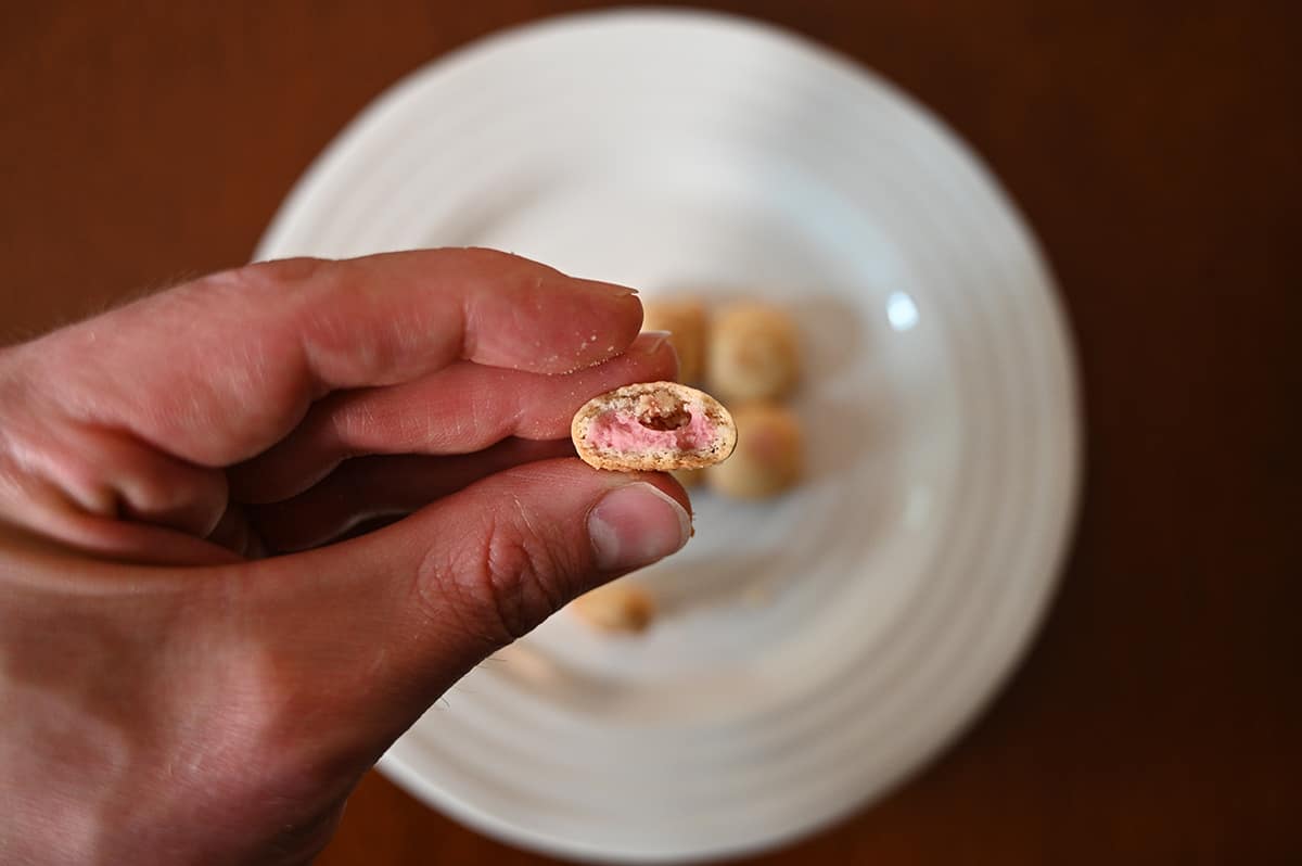 Image of a hand holding one Hello Panda cookie in front of the camera with a bite taken out so you can see the filling. There is a plate of cookies in the background.