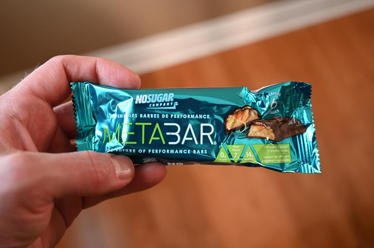 Image of a hand holding one individually wrapped protein bar in front of camera.