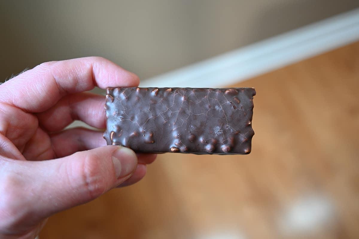 Image of a hand holding one protein bar unwrapped in front of the camera.