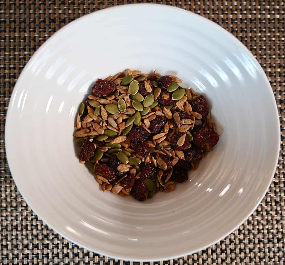 Top down image of the salad topper poured into a white bowl so you can see pumpkin seeds, sunflower seeds and dried cranberries.