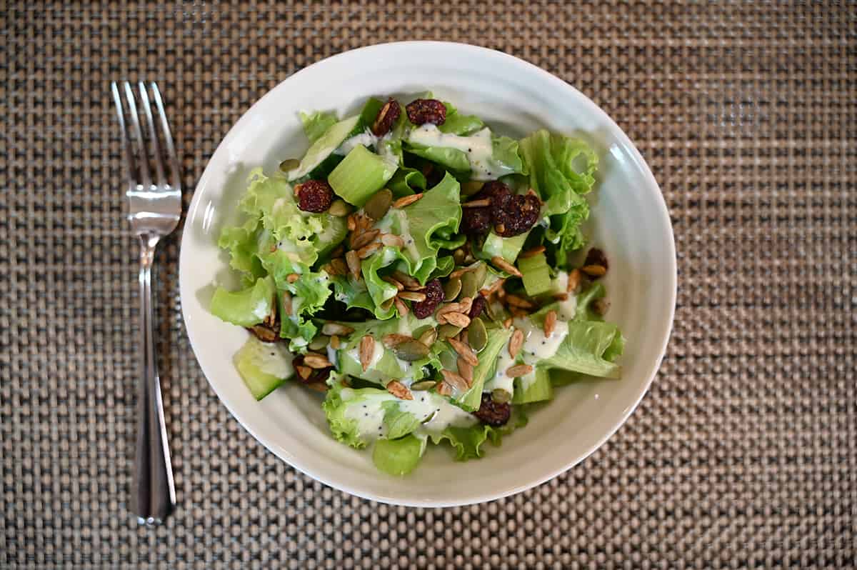 Top down image of a prepared garden salad in a white bowl. The salad topper is on the top of a bed of greens and there is a drizzle of creamy dressing.