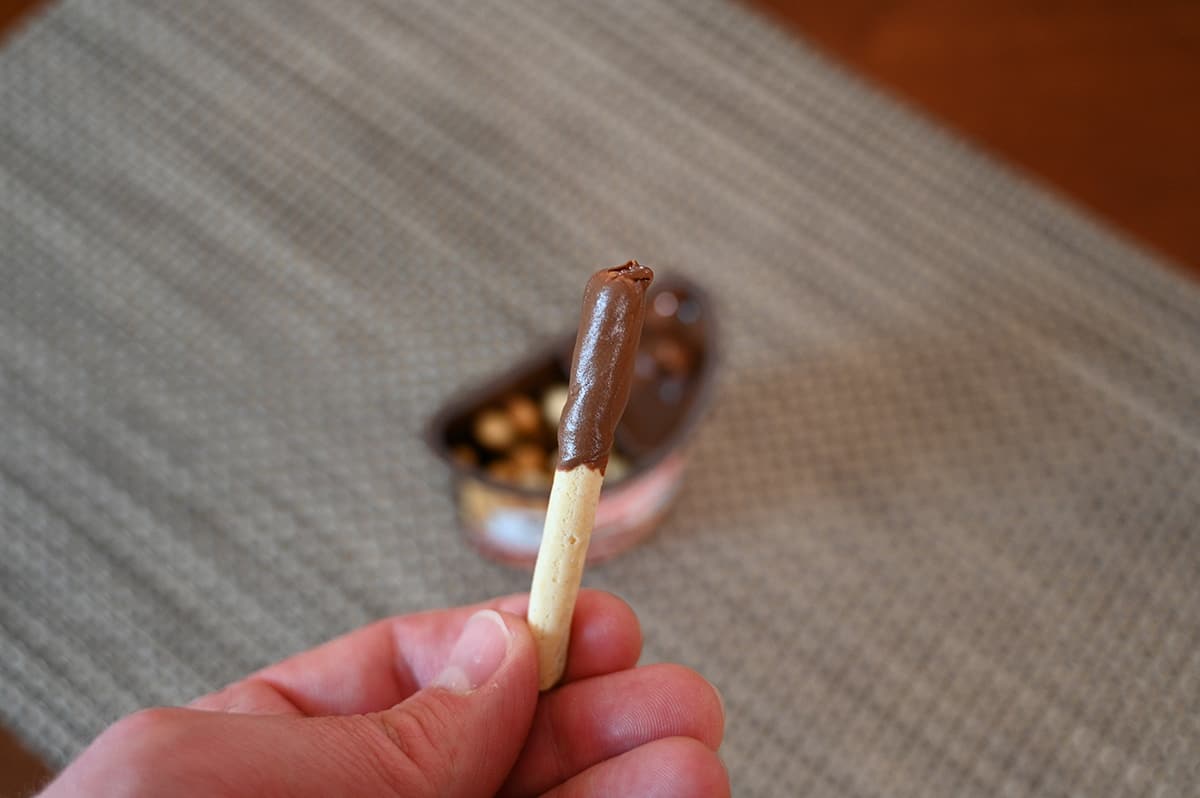 Closeup image of a hand holding one breadstick dipped in Nutella close to the camera with the package in the mm.
