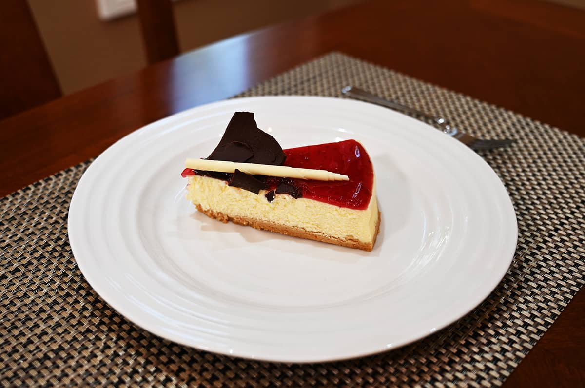 Image of one slice of cheesecake served on a white plate, sitting on a table.