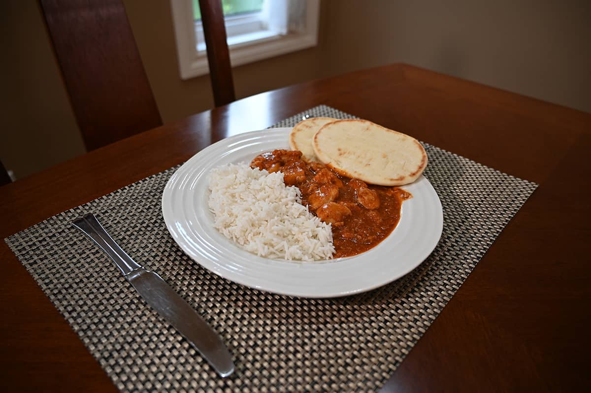 Sideview image of a plate of chicken vindaloo, rice and naan sitting on a placemat with a knife beside the plate.